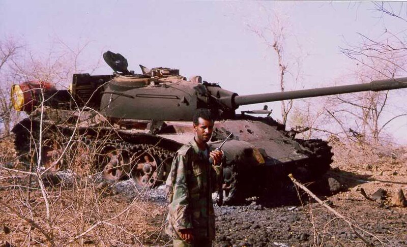 An Eritrean soldier stands in front of a destroyed T-55A tank in 1999. This war starts in 1998 but the mutual military build-up for it arguably started in 1996. (Broń Pancerna/Flickr)